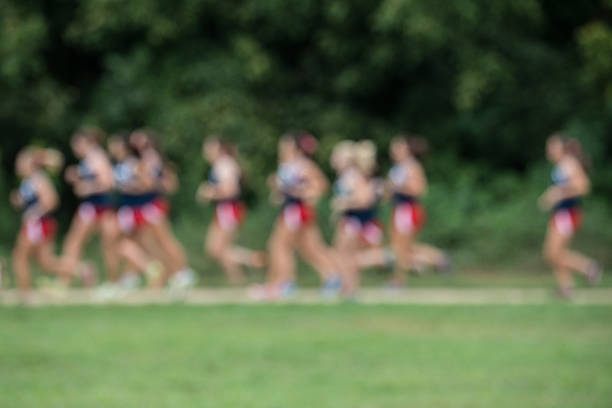 blurred image of a group of female cross country athletes running along a grassy trail