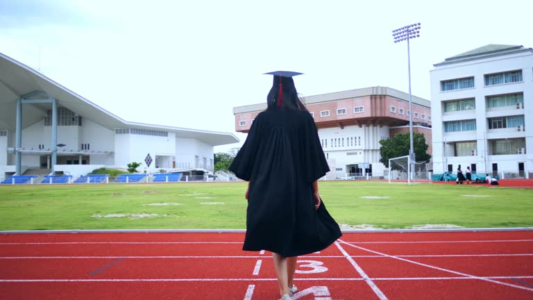 Female graduate walking across a running track